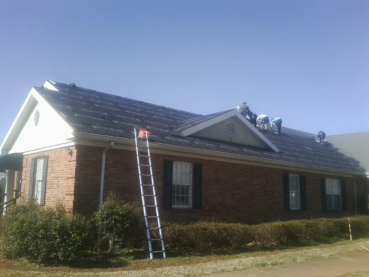 Crew tearing shingles off a brick ranch roof with a ladder set — Metal Roof Repair work by our crew in Marcola