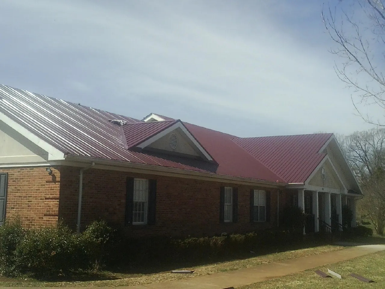 Red metal roof with gabled entries on a long brick building, from a Hail Damage Roof Repair job in Marcola