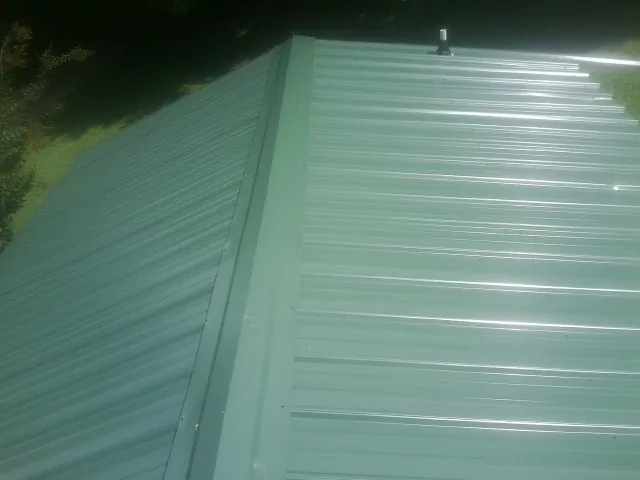 New green metal panels meeting at the ridge of a roof — Flat Roof Repair work by our crew in Marcola