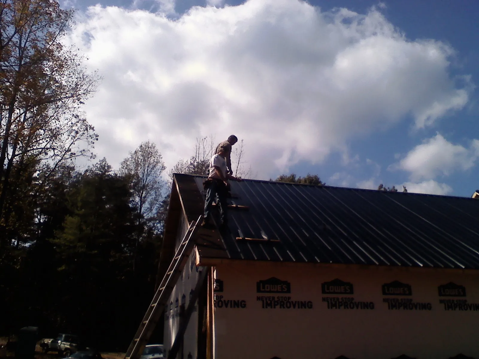Roofer fastening dark metal panels high against a cloudy sky, from a Roof Inspection job in Marcola