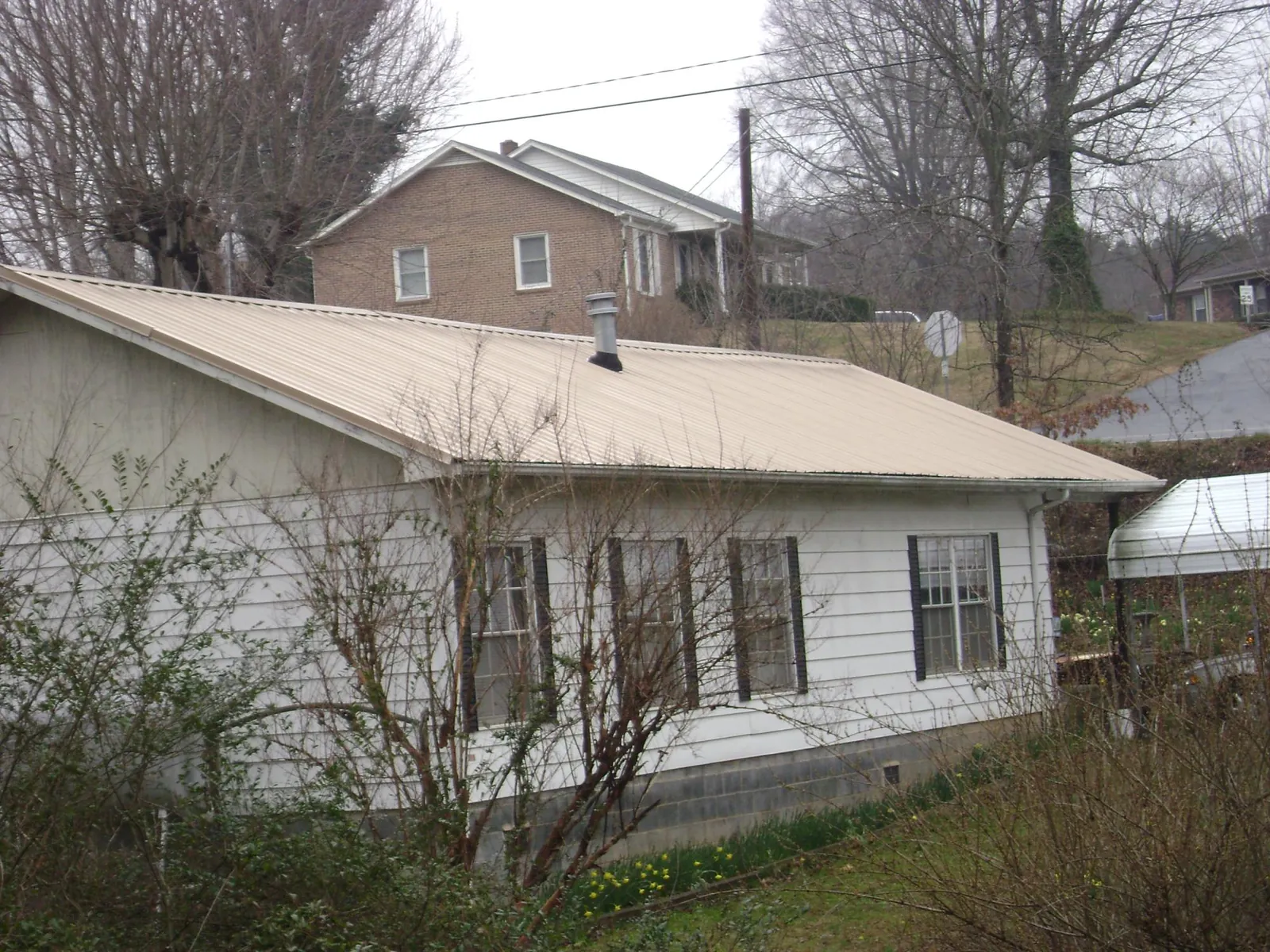 Tan metal roof on a white sided house set into a hillside — Commercial Roofing by Roofing Brothers in Marcola